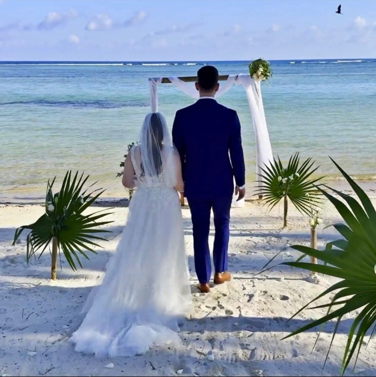 Bride and groom walking toward a white fabric wedding arch on a beach — intimate elopement